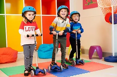 Three Children having fun on scooters in the play area.