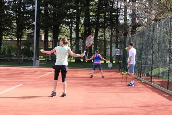 A tennis coach helps members improve their technique