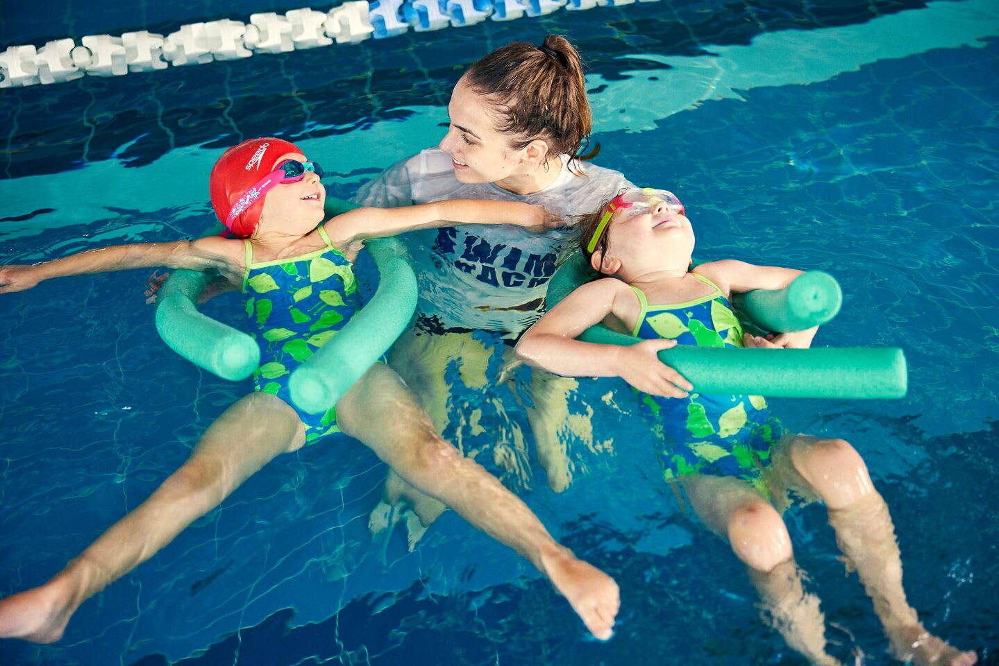 Swim coach with two kids using woggles