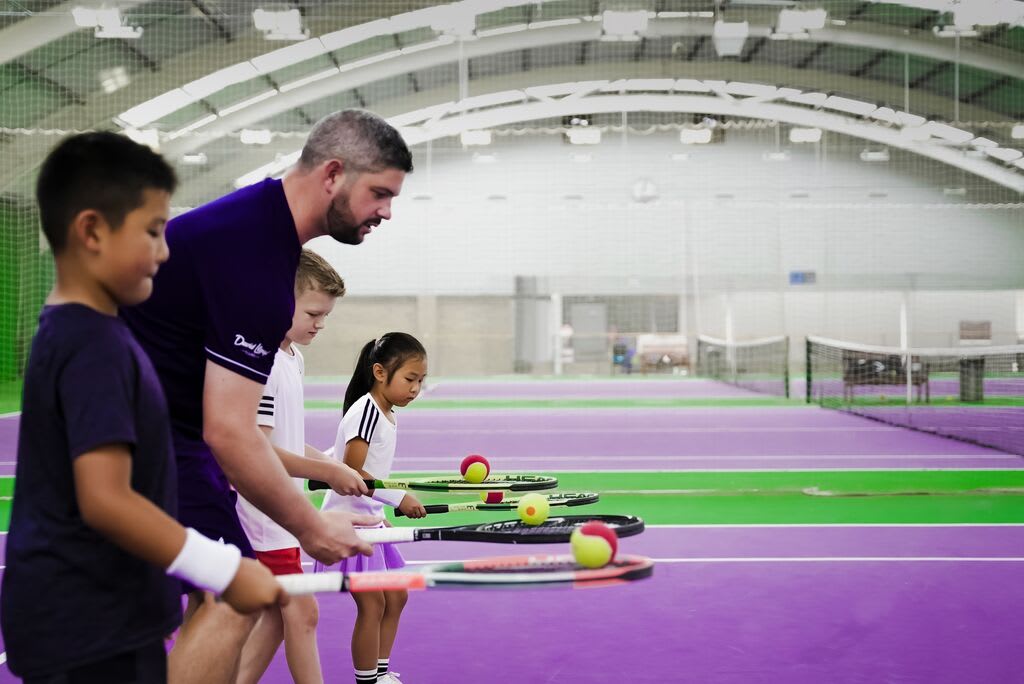 A man and a child on an outdoor tennis court.